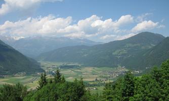 A picturesque mountain landscape with green valleys and snow-capped peaks. The sky is blue with some white clouds.