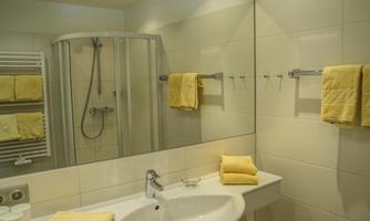 A modern bathroom with a shower and a white vanity. Yellow towels hang on the wall, and the walls are covered in light tiles.