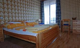 A cozy bedroom with a large wooden bed and colorful blankets. The walls are decorated with a striking pattern, and there is a view of the outdoor area through a window.