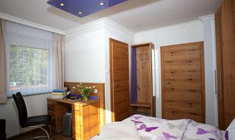 A cozy room with wood decor, a desk and a chair. The walls are light, and there is a large window with natural light.