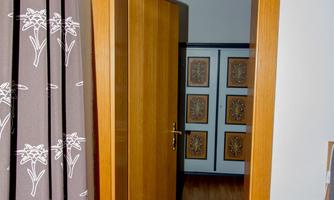An open wooden door leads into a room with pictures on the wall. The floor is made of wood, and a curtain is visible.
