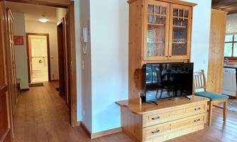 A cozy living room with a wooden cabinet and a television. The room has a bright, inviting atmosphere.