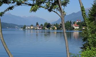 A tranquil lake landscape with clear water and surrounding mountains. In the background, colorful buildings and trees can be seen.