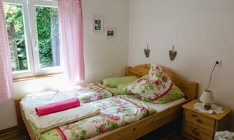 A cozy bedroom with a wooden bed and colorful bedding. The window lets in plenty of daylight and offers a view of the green surroundings.