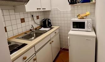 A small, functional kitchen with a sink, a stove, and a refrigerator.  
On the countertop, there are some kitchen appliances and dishes.