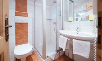 A modern bathroom with a shower, sink, and toilet. The walls are brightly tiled, and there are some towels ready.