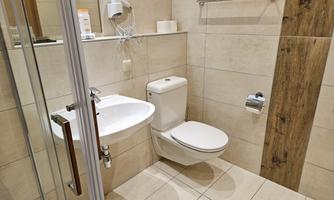 A modern bathroom with a shower, a toilet, and a sink. The walls are light tiled and there are wood details for a warm atmosphere.