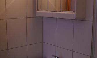 A small bathroom with a sink and a mirror. A towel is on the shelf.