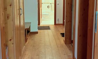 A bright hallway with wooden flooring and doors on both sides. At the end of the hallway, a room is visible.