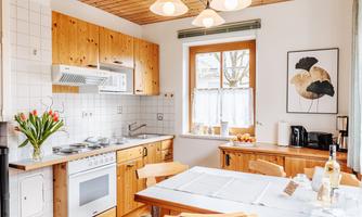 A cozy kitchen with wooden cabinets and a large window. Fresh flowers and fruit are on the table.