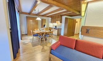 A cozy apartment with a wooden ceiling and modern furniture. The room features a dining area and a sitting area with a red sofa.