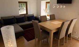 A modern living room with a cozy couch and a large dining table. The bright walls and warm light create an inviting atmosphere.