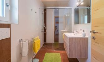 A modern bathroom with a shower and a sink. The features include bright tiles and towels in yellow.