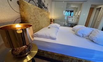 A modern bedroom with a upholstered bed and bright pillows. Next to the bed stands a stylish lamp.