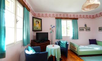 A cozy room with pink walls and blue curtains. There is a television, a table, and a single bed.
