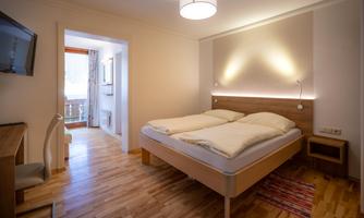 A modern bedroom with two single beds and wooden flooring. The room is bright and cheerful, with a window leading to a balcony.