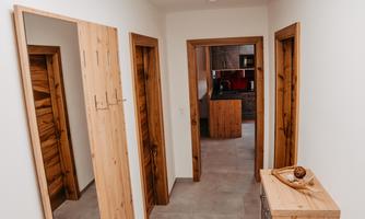 A bright hallway with wooden paneling and two doors on each side. At the end of the hallway is a modern kitchen.