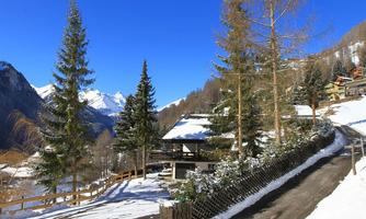 A picturesque winter landscape with snow-covered mountains and pines. A cozy chalet sits at the edge of a cobblestone path.