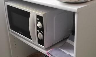 A small kitchenette with a microwave, a kettle, and a coffee pot. There are also paper towels and a basket on the shelf.