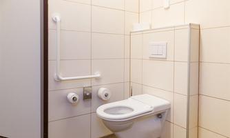 A modern bathroom with a toilet and a grab bar. The walls are tiled in light colors and the floor has a wood design.
