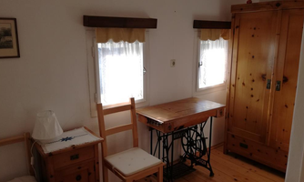 A simple room with wooden furniture and two windows. The room is bright and cozily furnished.