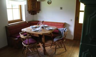 A cozy dining area with a wooden table and rustic chairs. The walls are light, and there is a bench with red cushions.