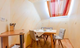 A cozy dining area with a wooden table and chairs. Bright walls and window decorations create a friendly atmosphere.