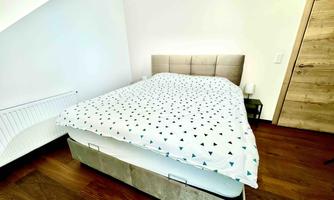A cozy bedroom with a large bed and a modern duvet. The floor is made of wood and the walls are painted light.