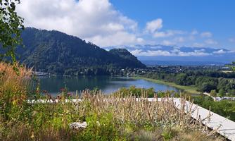 A picturesque landscape with a lake and gentle hills. The sky is clear and blue with a few clouds.