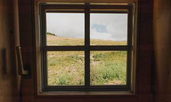 A view from a window onto a green meadow and a cloudy sky. The scene conveys a sense of tranquility and nature.