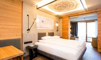 A modern hotel room with a double bed and wooden elements. The room is bright and cozy, with a table and chairs.