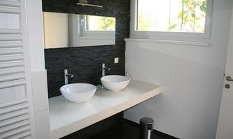 A modern bathroom with two elegant sinks on a white countertop. Large windows bring plenty of daylight into the room.