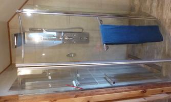 Glass shower under a sloped ceiling with shower panel, rain shower head, hand shower and massage jets; a blue towel hangs on the door.