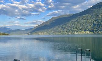A tranquil lake with mountains in the background and a fast-moving cloud cover. A bench stands at the shore, perfect for relaxation.