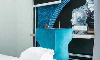 A stylish room with a blue armchair and modern art on the wall. Freshly folded towels are placed on the bed.