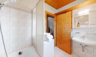 A modern bathroom with a bathtub and a separate shower. There is a wooden ceiling and a sink with a mirror cabinet.