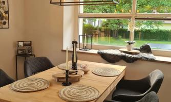 A modern dining area with a wooden table and stylish black chairs. The large window lets in plenty of daylight and the room is decorated with cozy decor.