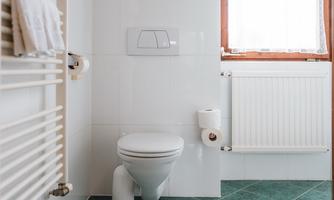 A modern bathroom with green tiles. Visible are a toilet, a towel rack, and a window with a curtain.