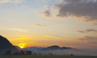 A picturesque sunrise over hills with a light fog in the foreground. The sky is painted in soft shades of yellow and orange.