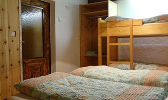 A simple bedroom with a bunk bed and a single bed. The walls are made of wood and a door leads outside.