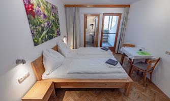 A bright bedroom with two single beds and wooden furniture. In the background, there is access to a small balcony.