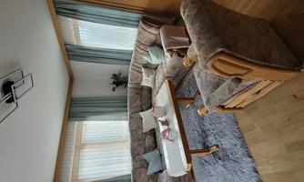 A cozy living room with a large couch and a coffee table.  
Plenty of daylight streams through the windows, and the rooms are accented with curtains.