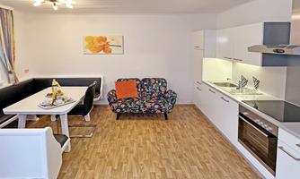 A modern apartment with an open kitchen and a dining area. The cozy living area is furnished with a colorful sofa and a table.