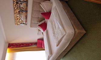 A cozy bedroom with a large double bed and red pillows. The room has big windows and a decorative wall mural.