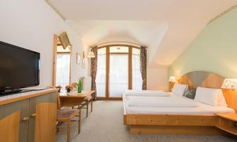 A cozy hotel room with two single beds and a television. Large windows provide plenty of daylight and a friendly atmosphere.