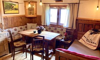 A cozy room with wooden furniture and an inviting seating area. The window lets in a lot of daylight and the decoration creates a warm atmosphere.