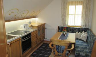 A cozy kitchen with wooden elements and a modern cooking area. There is a small floral decoration on the table and a bench with cushions.