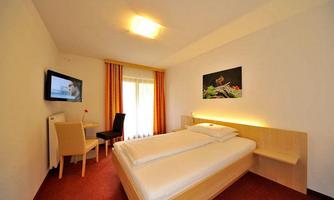 A modern hotel room with a double bed and a television. The windows are fitted with curtains, and the room has a bright, inviting feel.