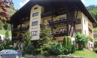 A cozy hotel with several balconies and beautiful plants. The surroundings are green and inviting.
