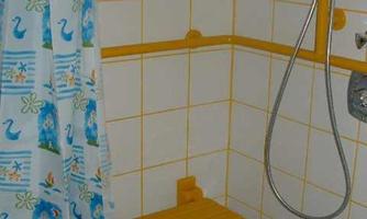 A shower area with yellow tiles and a shower rod. The shower curtain features a friendly pattern with ducks.